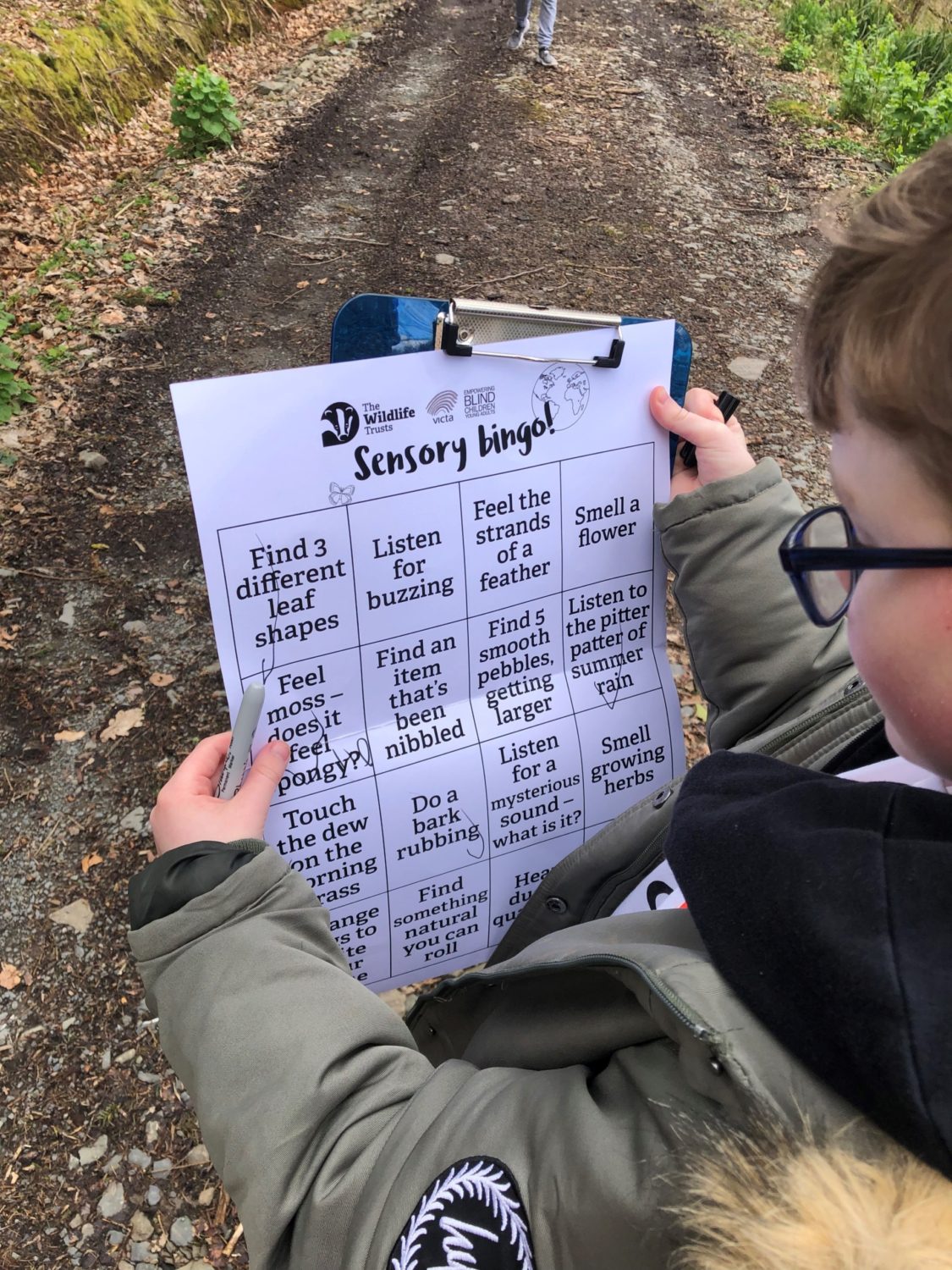 a child holds up a large print version of the sensory bingo