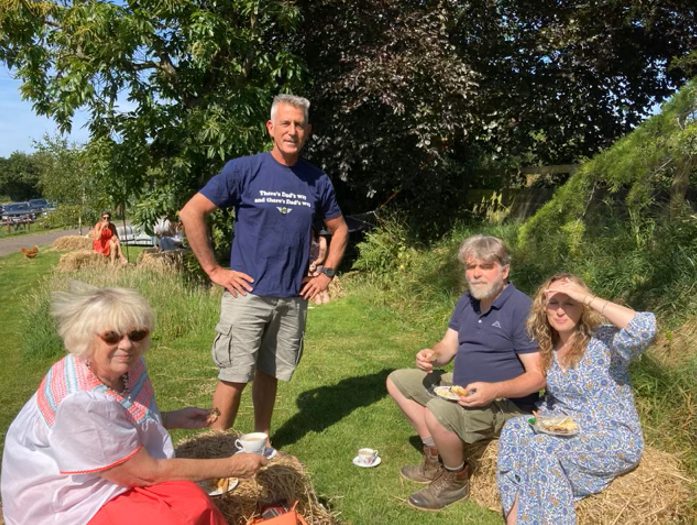 Guests sitting on hay bails in the garden chatting and eating cakes